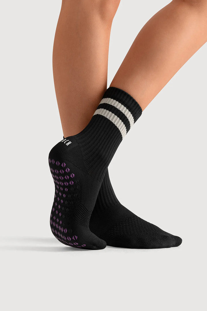 Black socks with white stripes and purple patterns worn by a person on a light gray background