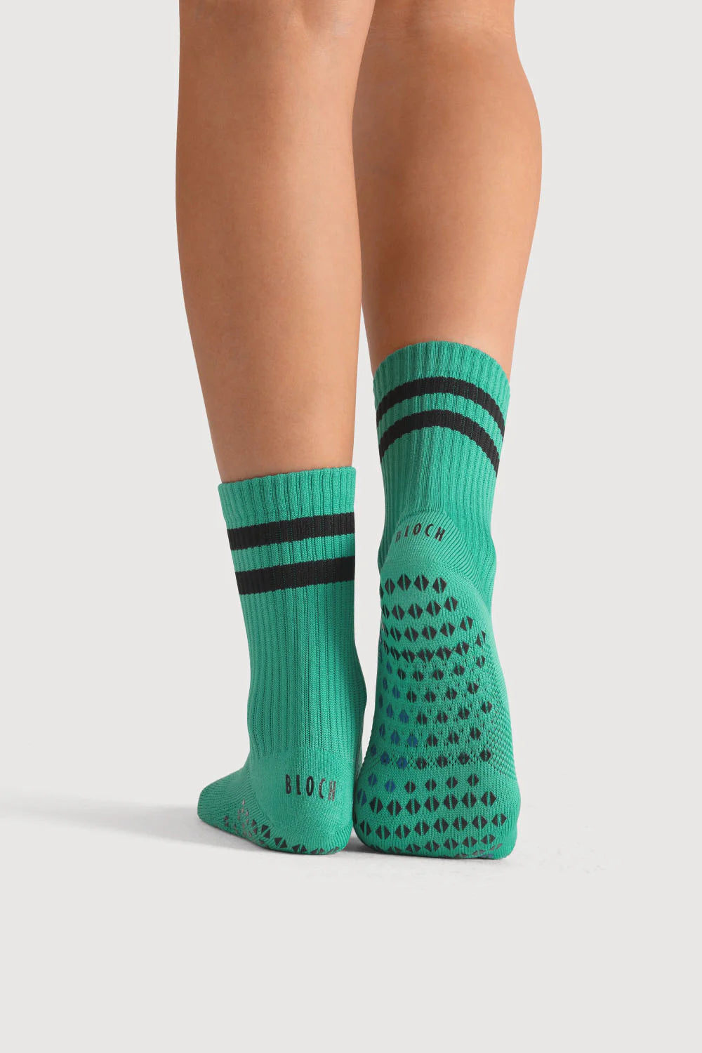 Green socks with black patterns and stripes worn by a person on a light gray background