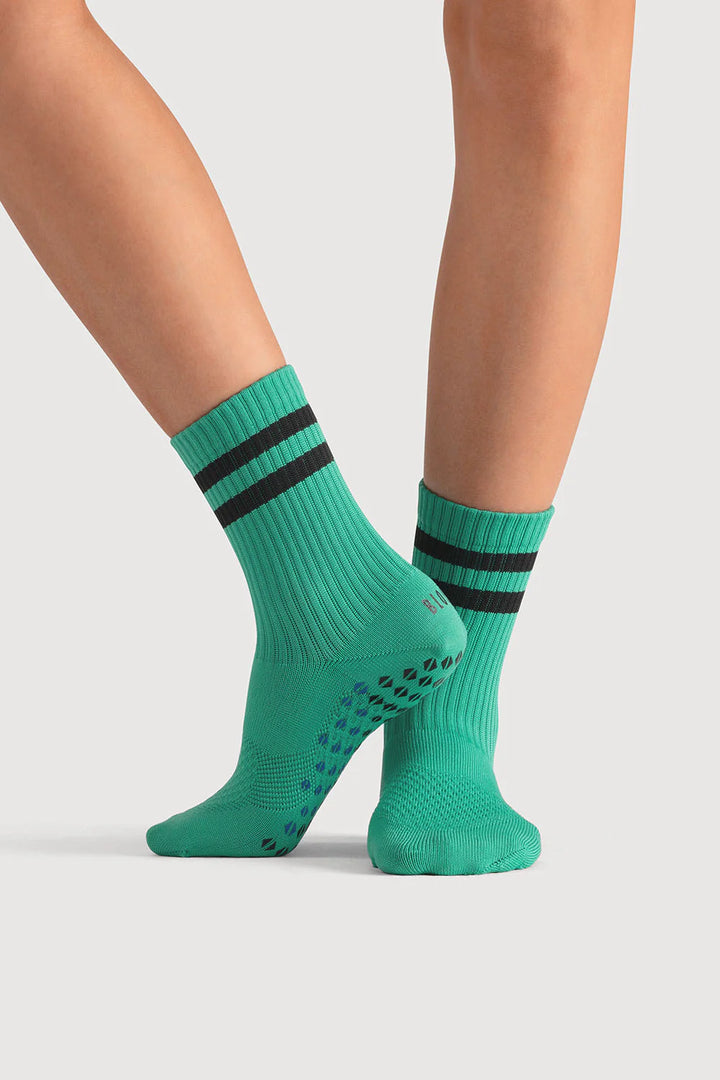 Green socks with black stripes worn by a person on a light gray background