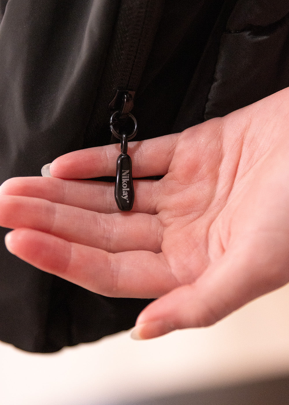 Hand holding a black keychain with a visible brand logo against a neutral background