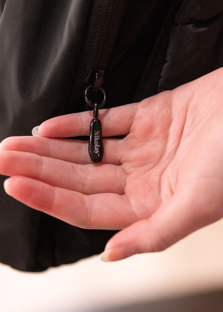 Hand holding a black keychain with a visible brand logo against a neutral background