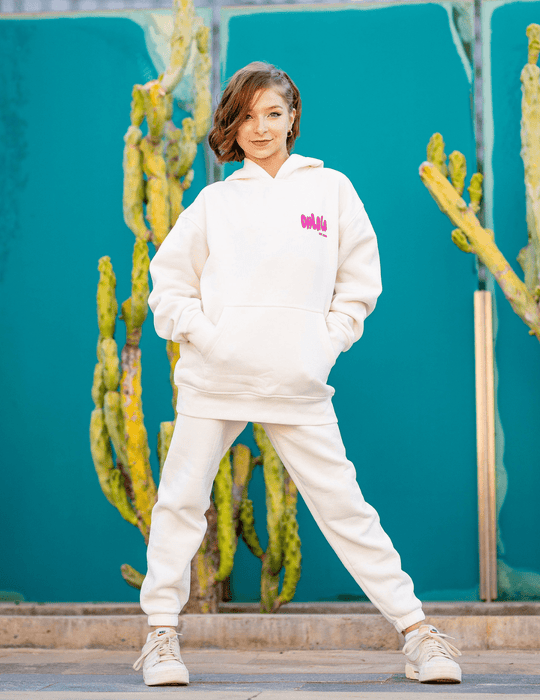 Person wearing a white hoodie with pink text in front of cacti