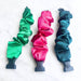 Three colorful scrunchies in green, pink, and blue on a white background