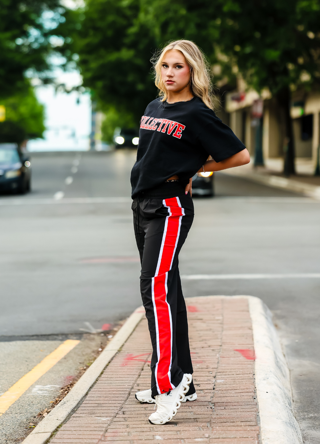Person wearing a black t-shirt and black pants with red stripes on a street.