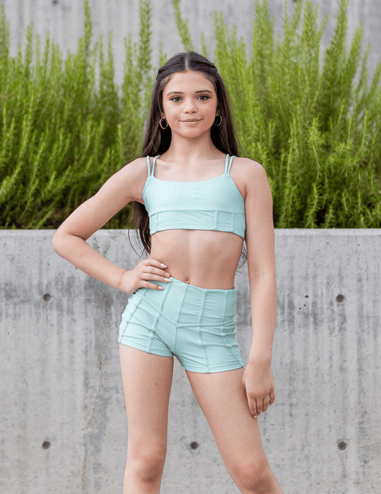 Woman wearing a light blue athletic outfit standing outdoors with greenery in the background
