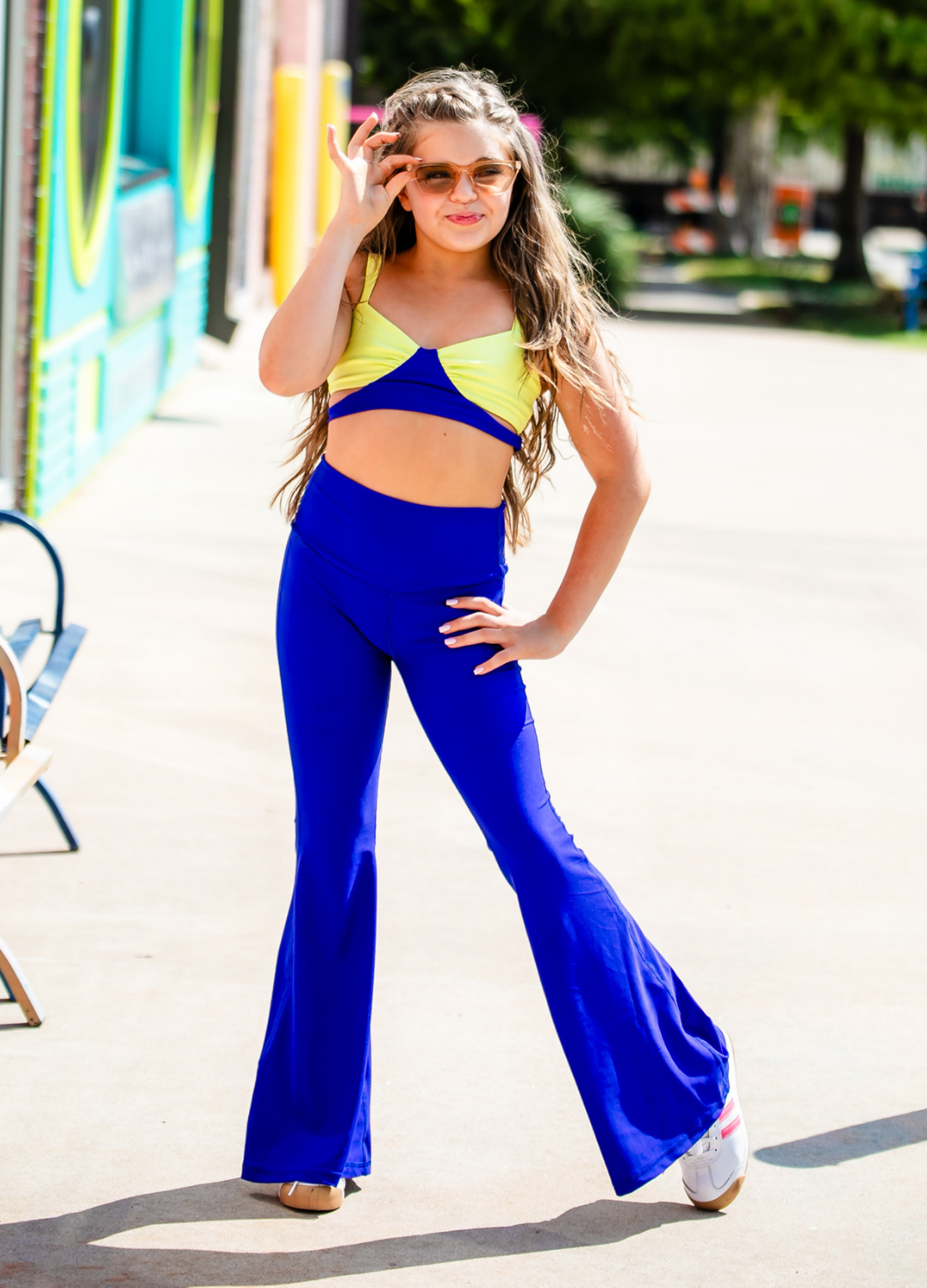 Woman wearing a yellow top and blue flared pants outdoors.