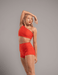 Woman wearing a red one-shoulder top and shorts against a gray background