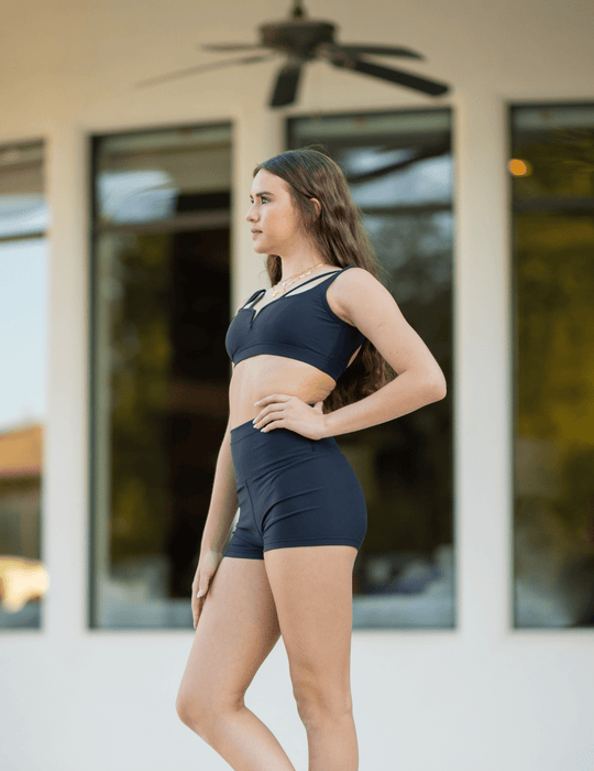 Woman wearing a navy athletic outfit standing in front of a house with large windows.