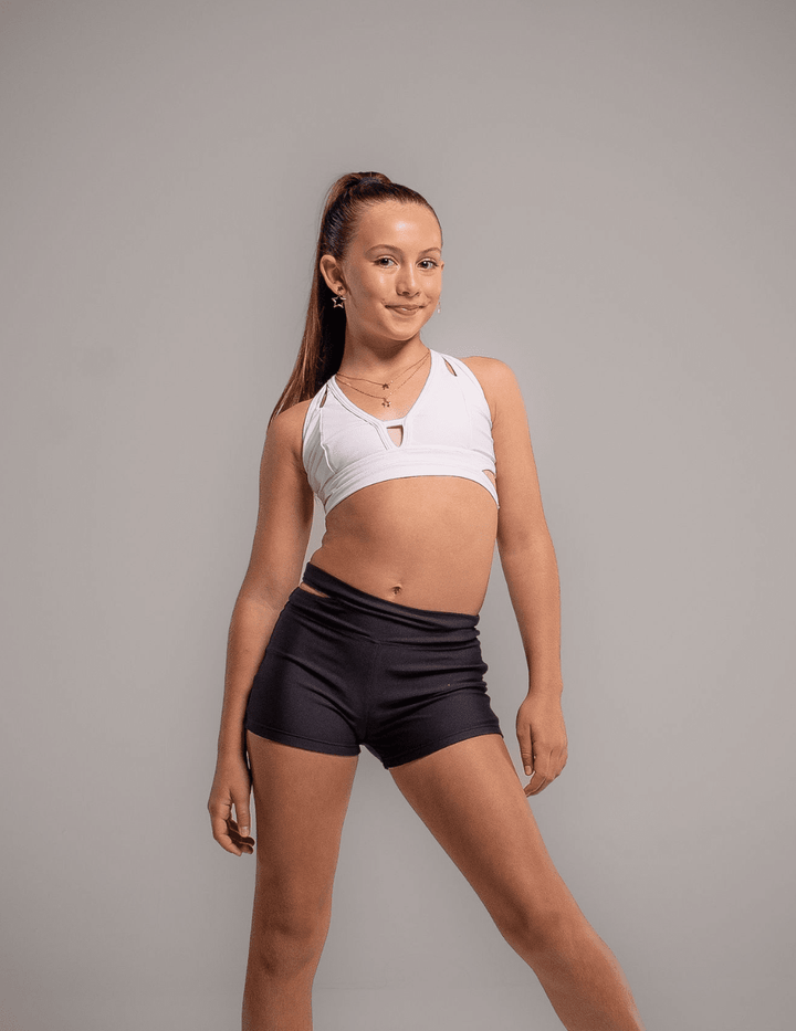 Woman wearing a white sports bra and black shorts on a gray background