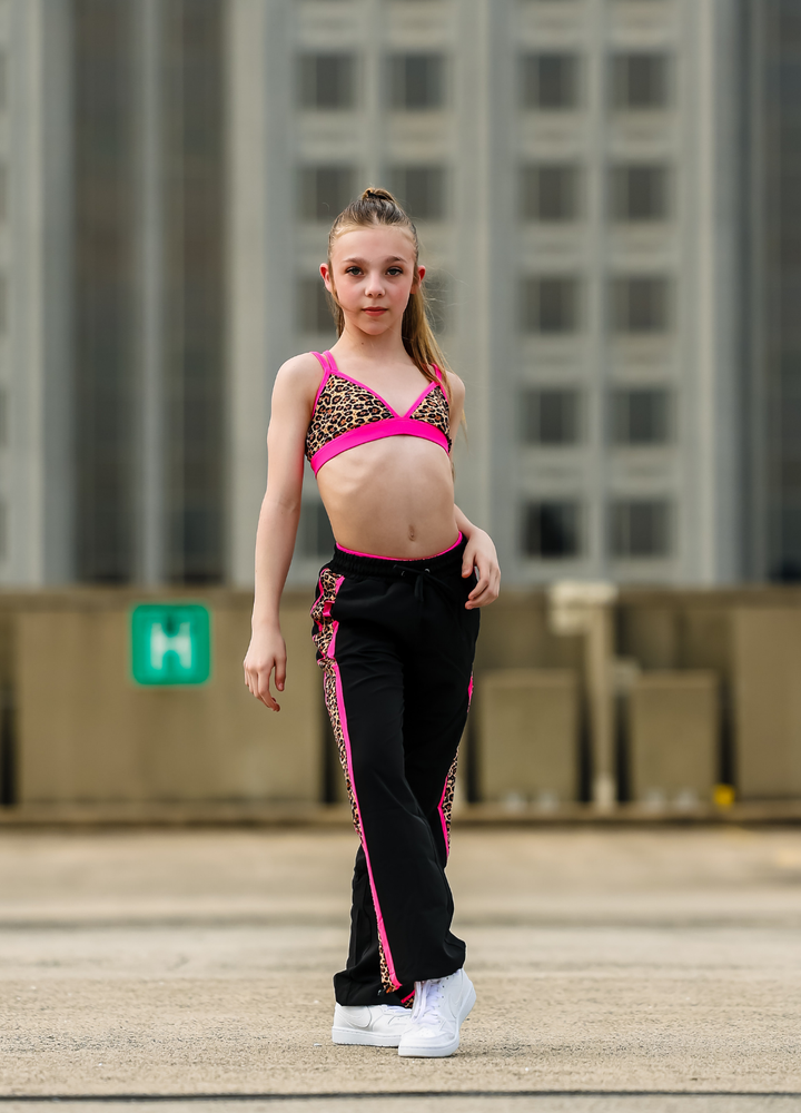 Young girl in a pink top and black pants with pink trim standing outdoors.