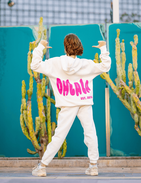 Person wearing a white hoodie with pink text in an outdoor setting with cacti.