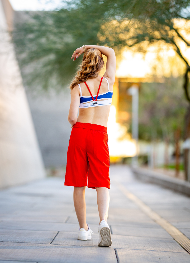 Woman in red shorts and sports bra walking on a wooden path with blurred background