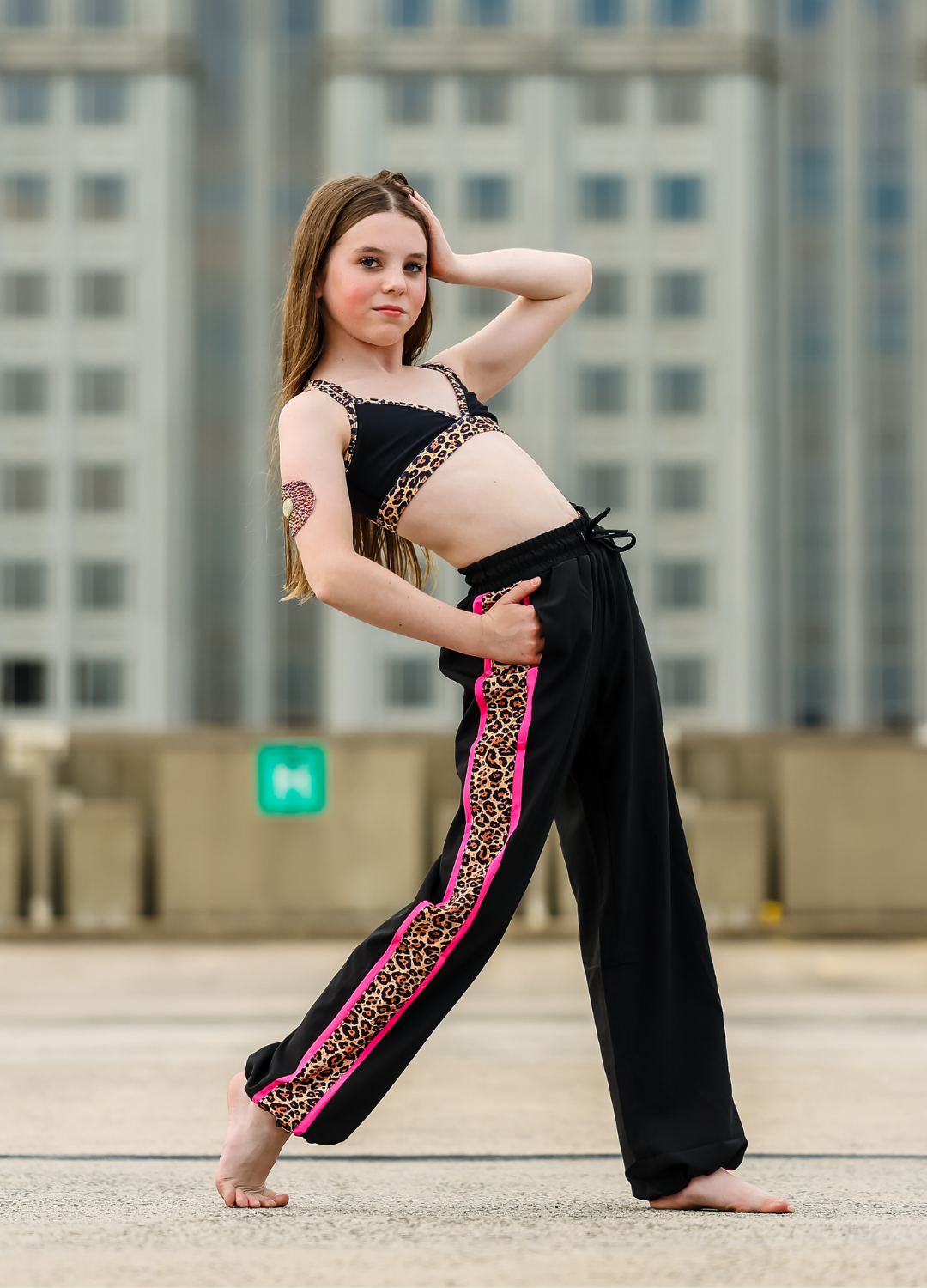 Young girl in a black and leopard print outfit standing on a rooftop with cityscape background