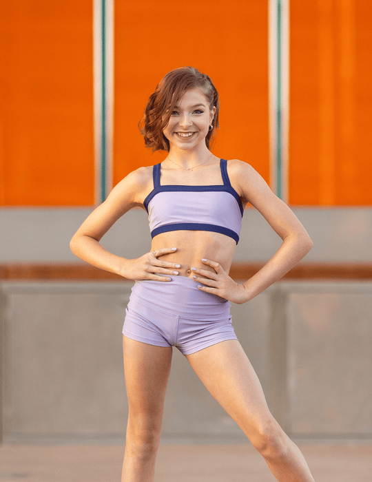 Woman in purple athletic wear posing against an orange wall.