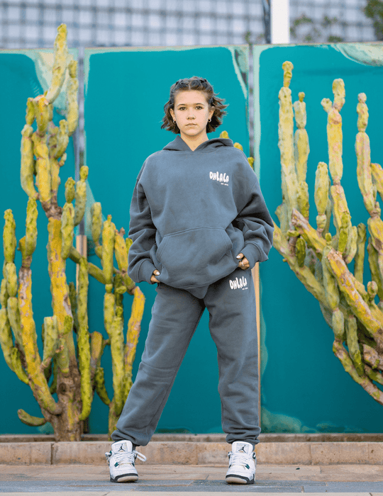 Person wearing a gray hoodie and pants with 'OBEY' logo in front of cacti