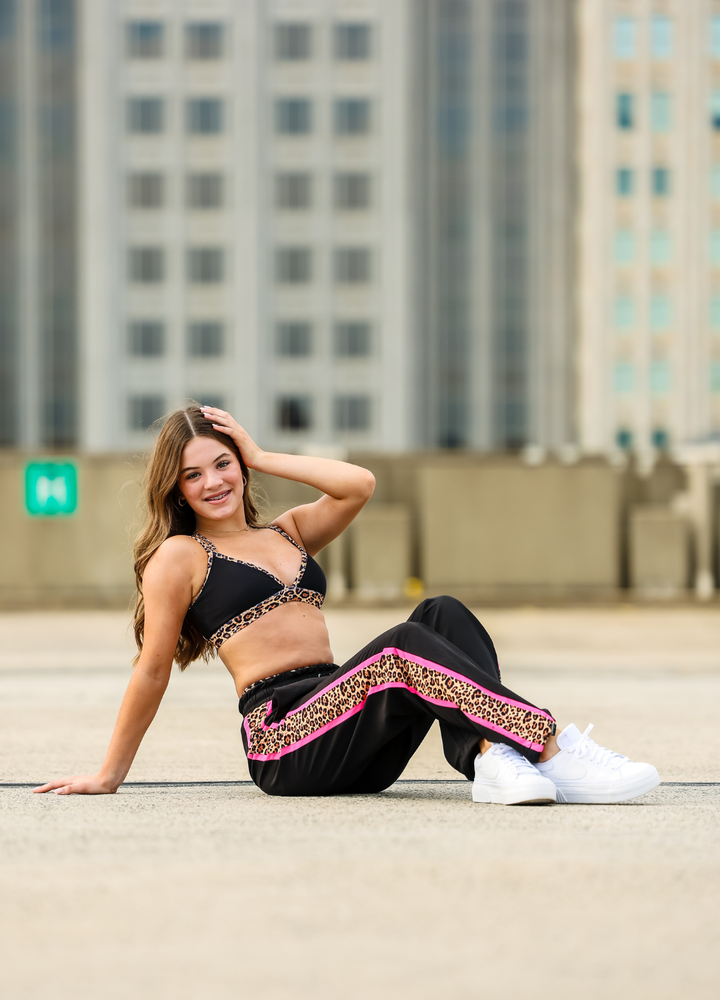 Woman in black and pink outfit sitting on a concrete surface with buildings in the background