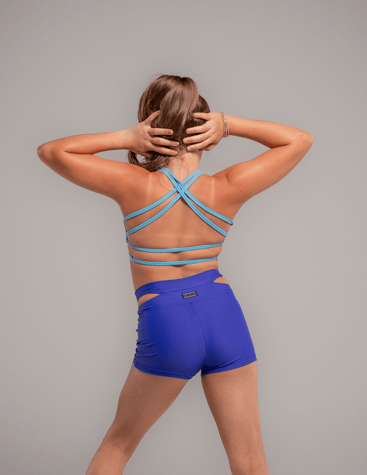 Woman wearing a blue sports bra and shorts on a gray background