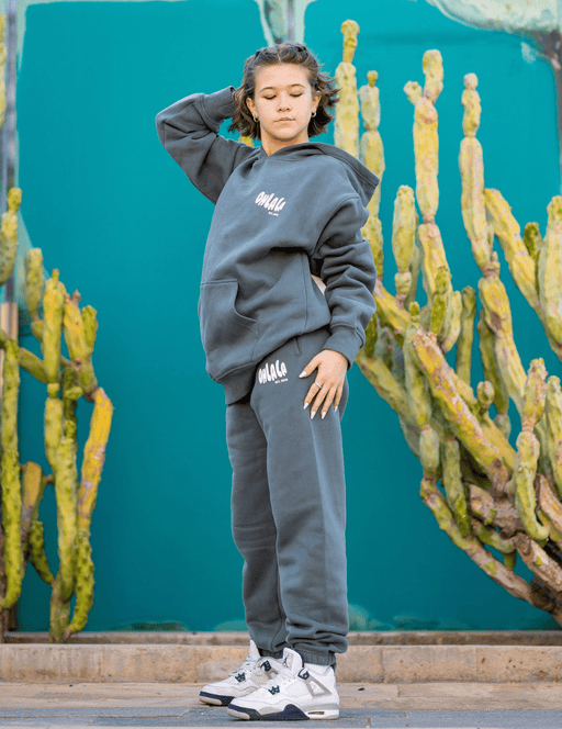 Person wearing a gray hoodie and pants with visible branding, standing in front of cacti.