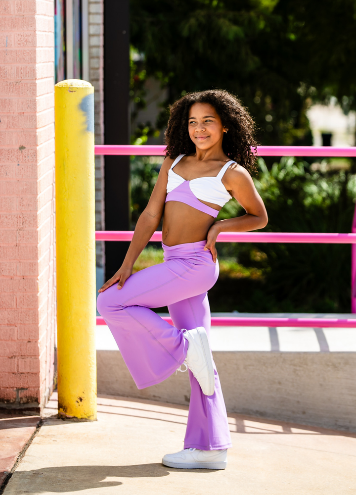 Woman in a white top and purple pants posing outdoors near a pink railing.