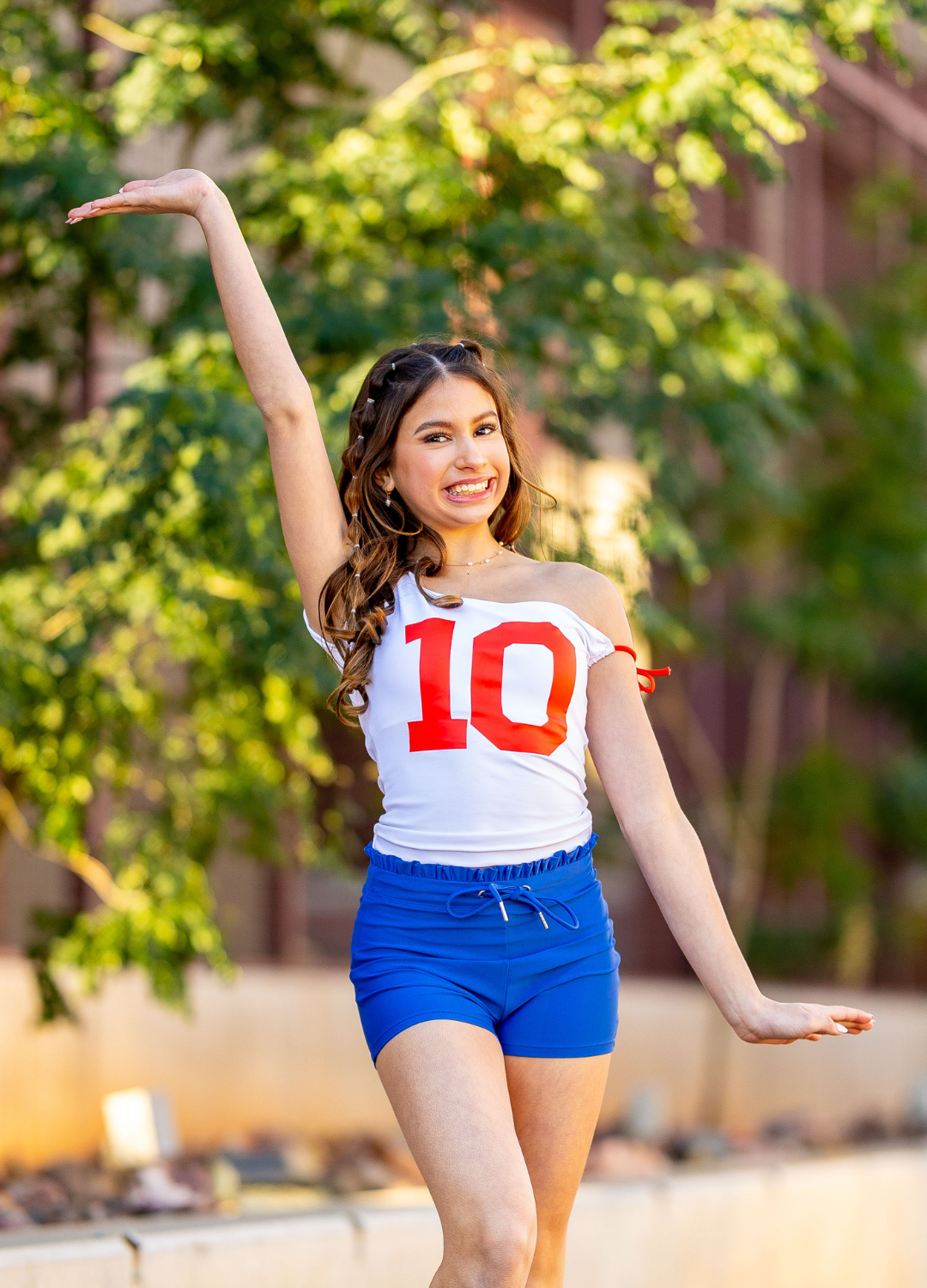 Woman in a white tank top with red number '10' and blue shorts posing outdoors.
