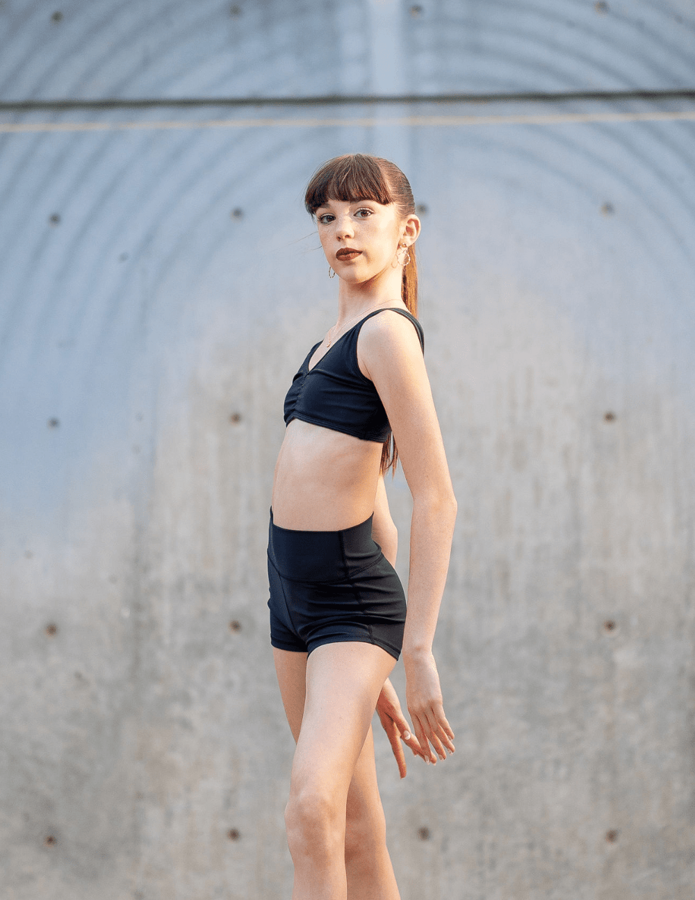 Young woman in black athletic wear standing against a gray wall.
