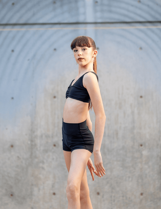 Young woman in black athletic wear standing against a gray wall.