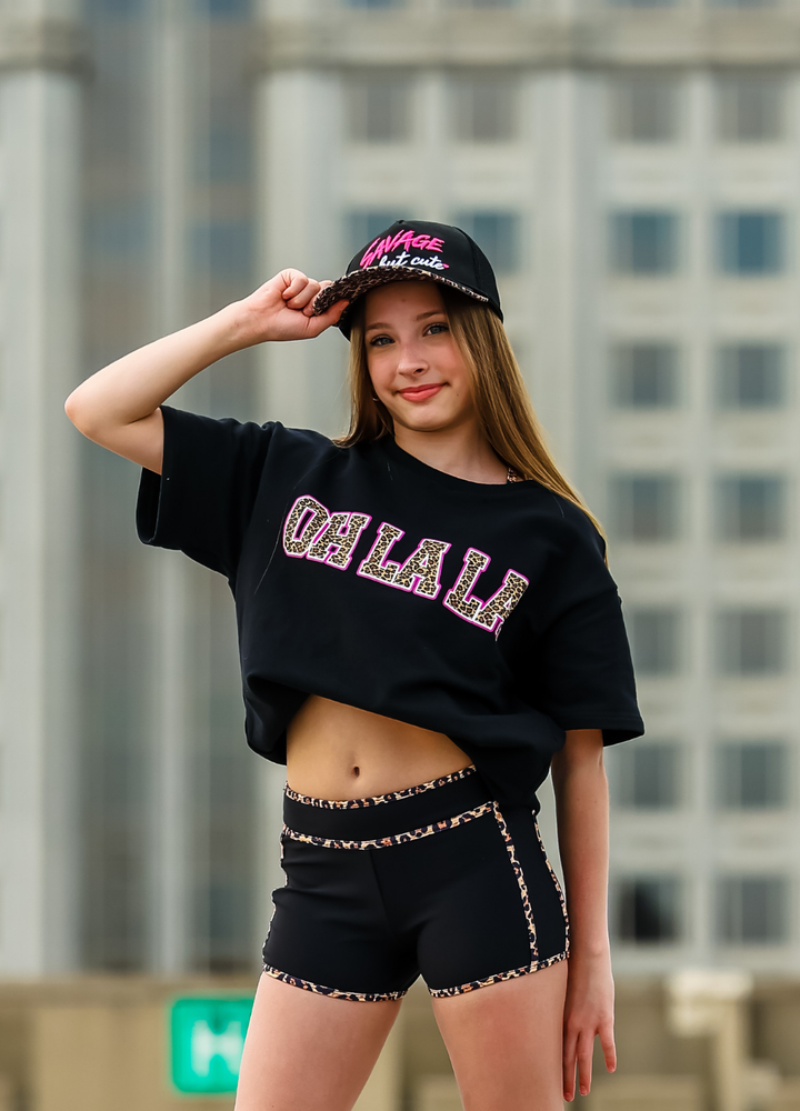 Person wearing a black crop top with colorful text and black shorts, standing in an urban setting.