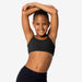 Young girl in a black sports bra and leggings stretching against a plain background