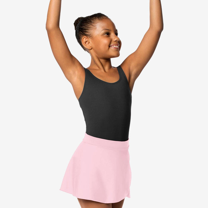 Young girl in a black tank top and pink skirt posing with arms raised on a white background