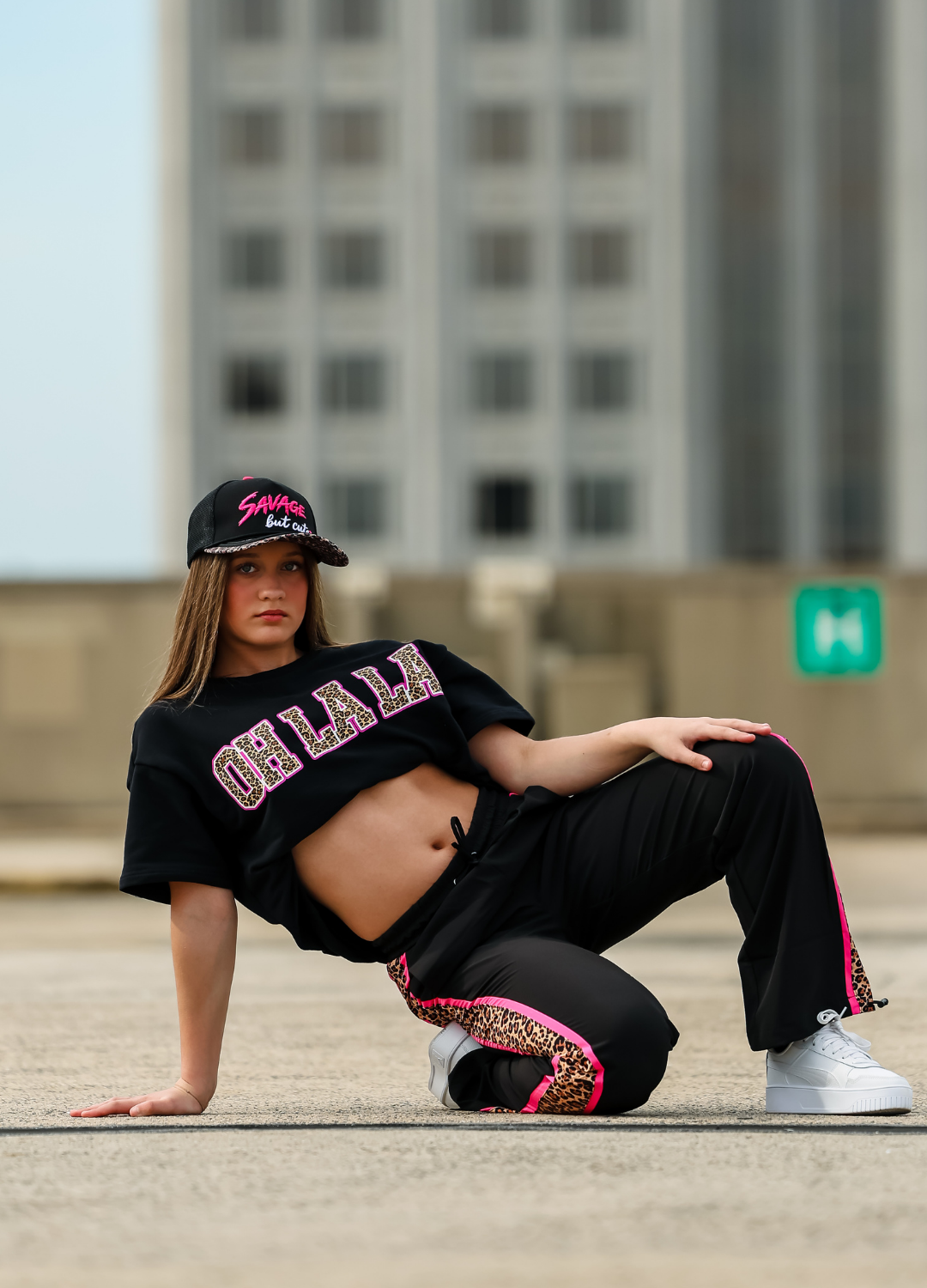 Person in black outfit with pink text and graphics on a city street background