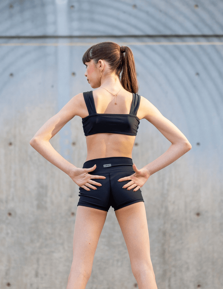 Woman wearing a black sports bra and shorts against a gray wall.