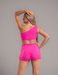 Woman wearing a bright pink one-shoulder top and shorts set against a gray background