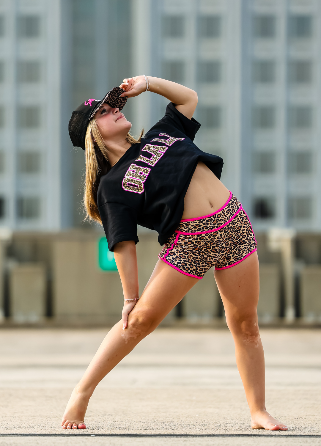 Person in black crop top and leopard print shorts with pink accents posing outdoors.