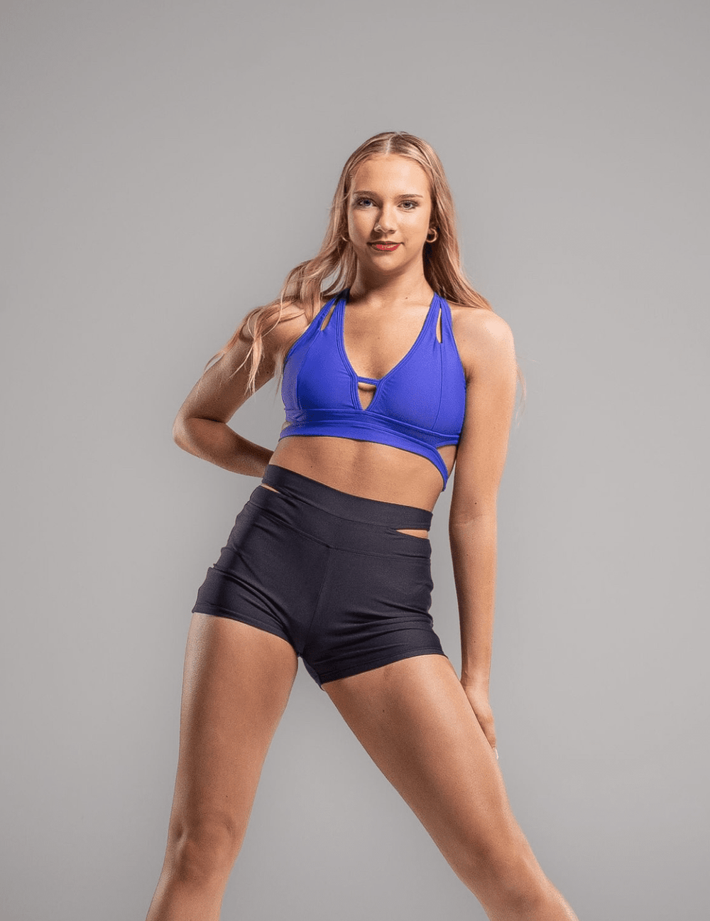 Woman wearing a blue sports bra and black shorts on a gray background