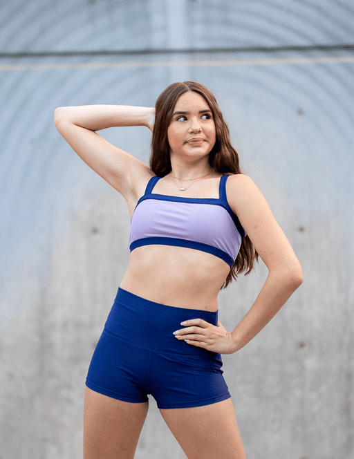 Woman wearing a purple sports bra and blue shorts against a neutral background