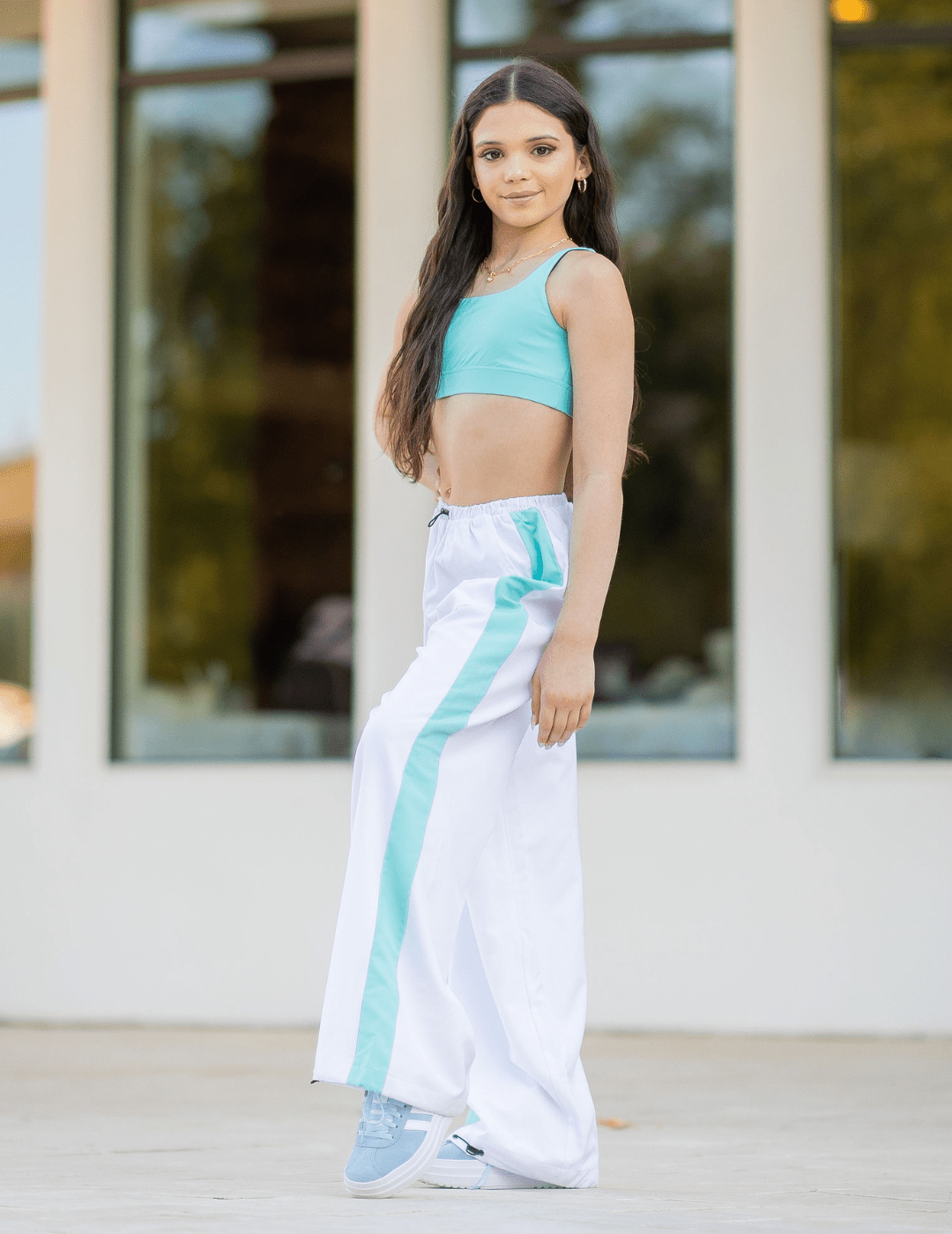 Woman wearing a turquoise top and white pants with blue stripes outdoors.