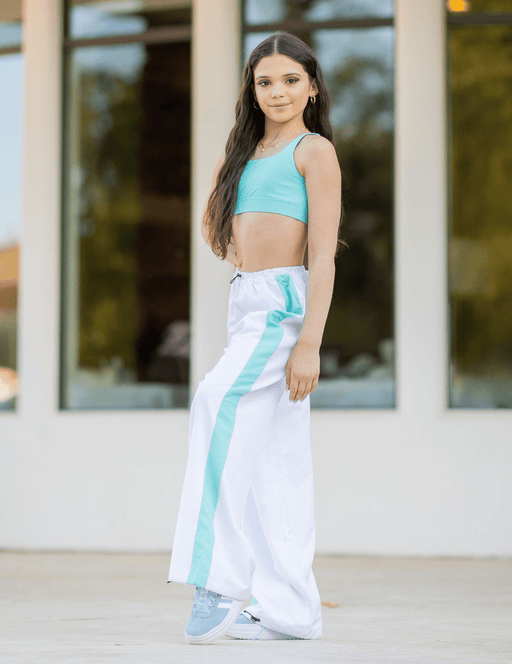 Woman wearing a turquoise top and white pants with blue stripes outdoors.
