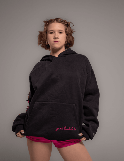 Person wearing a black hoodie with pink text on a gray background