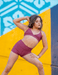 Woman in maroon athletic wear posing against a colorful geometric background