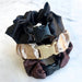 Three scrunchies in black, beige, and brown with metal clasps on a white background