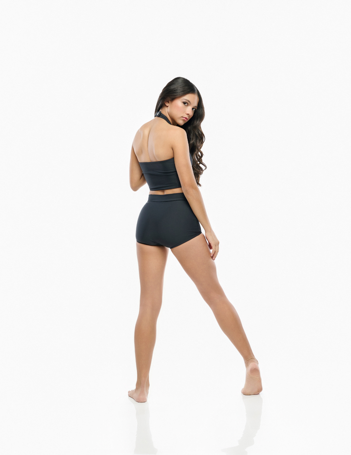 A woman modeling a black two-piece activewear set consisting of a strapless bandeau crop top and matching high-waisted shorts, shown from a rear three-quarter angle against a solid white studio background.