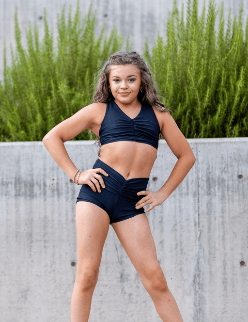 Woman in black athletic outfit posing outdoors with greenery in the background