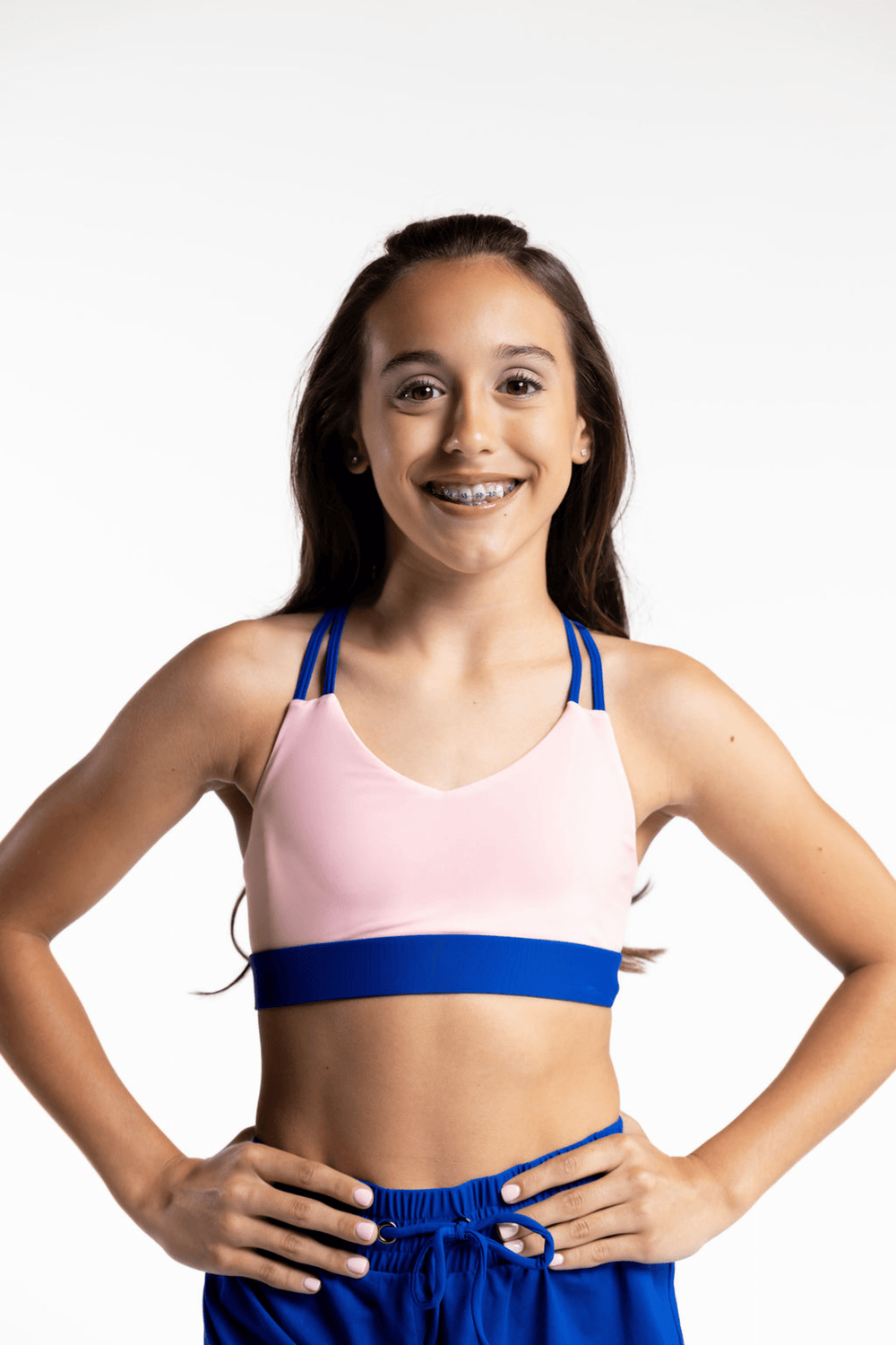Young girl wearing a pink sports bra and blue shorts on a white background