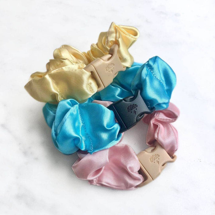 Set of three satin scrunchies in gold, blue, and pink on a white background