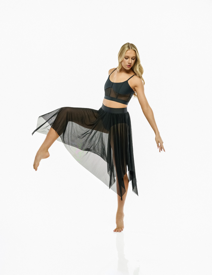 A woman modeling a black sheer mesh activewear set consisting of a sports bra and a high-waisted, flowing maxi skirt, posed against a solid white studio background.
