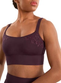 Woman wearing a dark purple sports bra with lace details on a white background