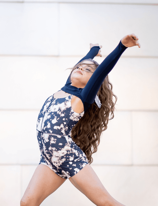 Woman in a navy long-sleeve top and camouflage shorts posing against a white wall.