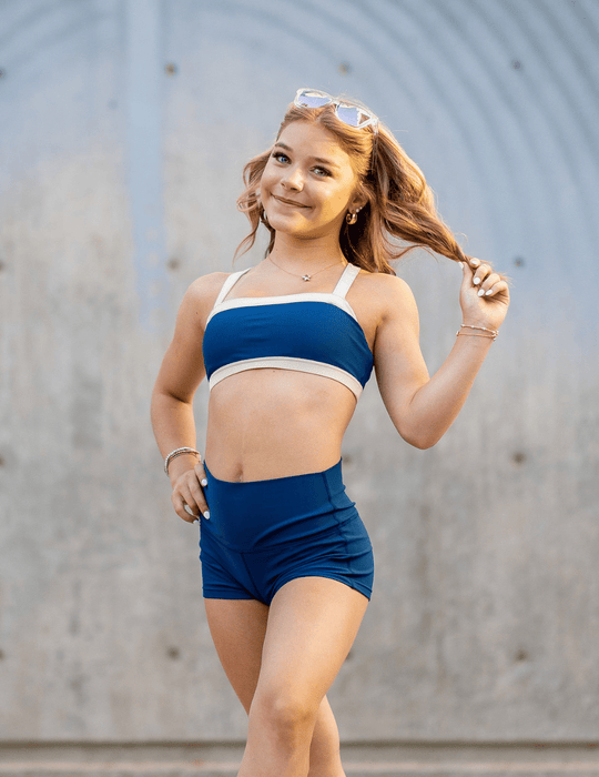 Young girl in a blue sports bra and shorts posing against a neutral background