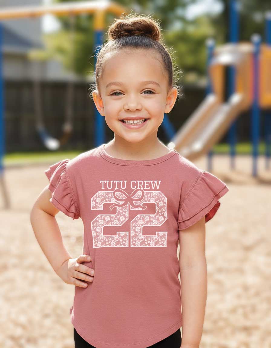 Young girl wearing a pink shirt with 'Tutu Crew 22' design on a playground.