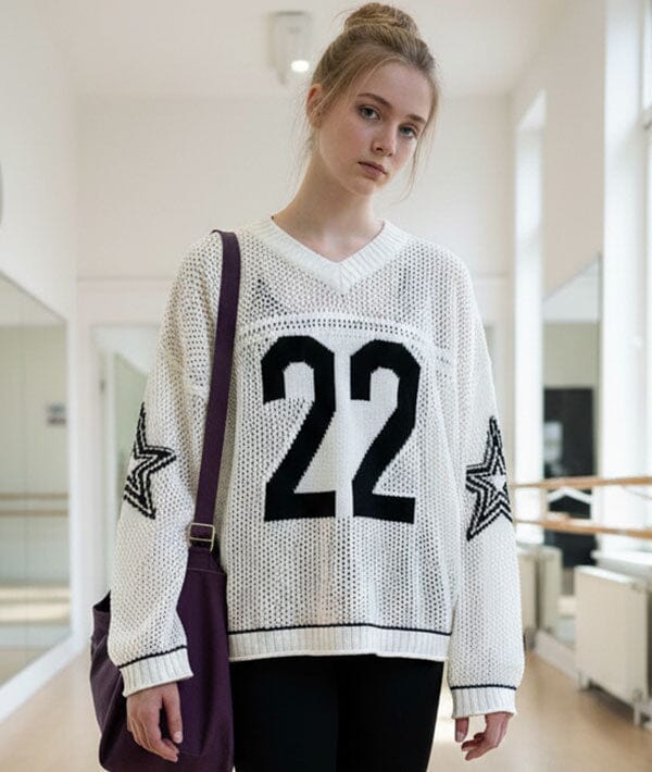 Woman wearing a white sweater with black numbers and stars indoors